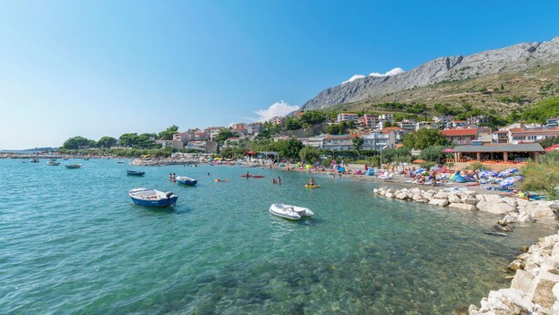 A coastal town with clear waters, boats, and a rocky shoreline. - Apartment Neda (Duce)