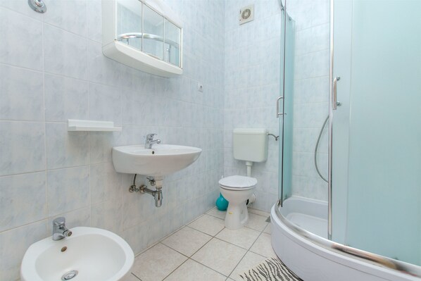 A bathroom with a sink, toilet, bidet, and a glass-enclosed shower.