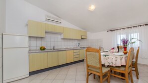 A kitchen with a dining area, featuring a refrigerator, cabinets, a sink, and a table set for dining. - Apartment Neda (Duce)