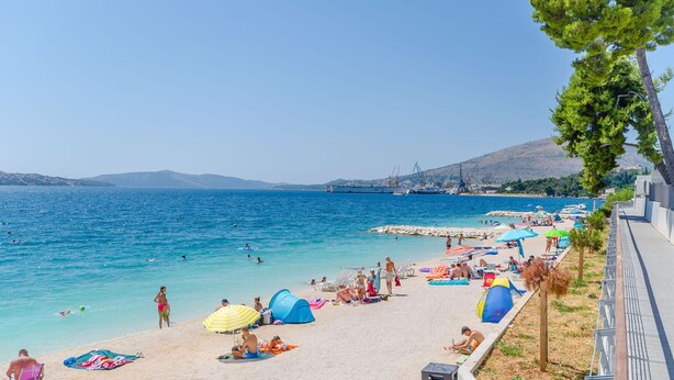 Una playa con gente tomando el sol, tiendas de campaña y sombrillas.