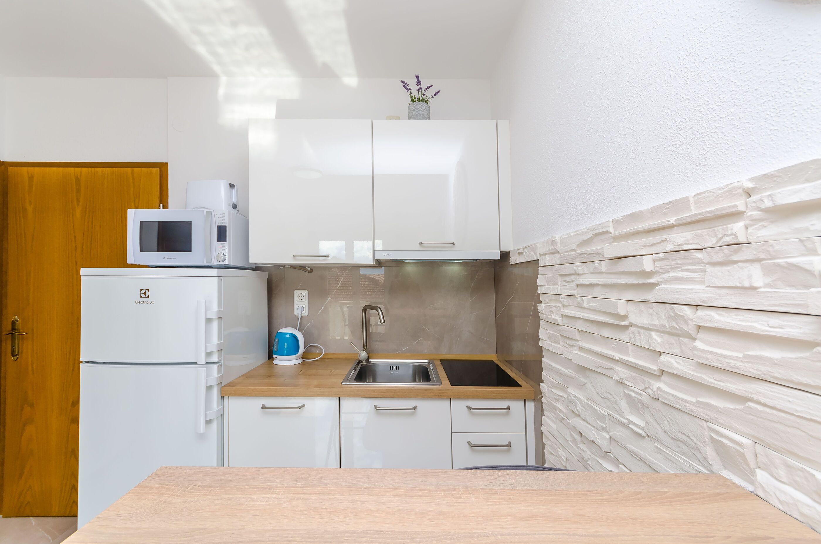 Een kleine keuken met witte kastjes, een magnetron, een broodrooster en een spoelbak.