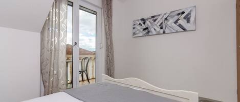 A bedroom with a bed, a view to a balcony, and a piece of abstract art on the wall.