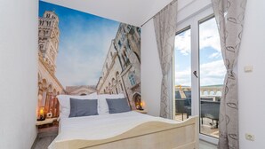 Un dormitorio con cama, mesita de noche, lámpara y vista a un paisaje urbano a través de una puerta de cristal.