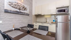 Una cocina moderna con armarios blancos, un refrigerador de acero inoxidable y un microondas. Hay una mesa de comedor con sillas y un adorno decorativo encima.