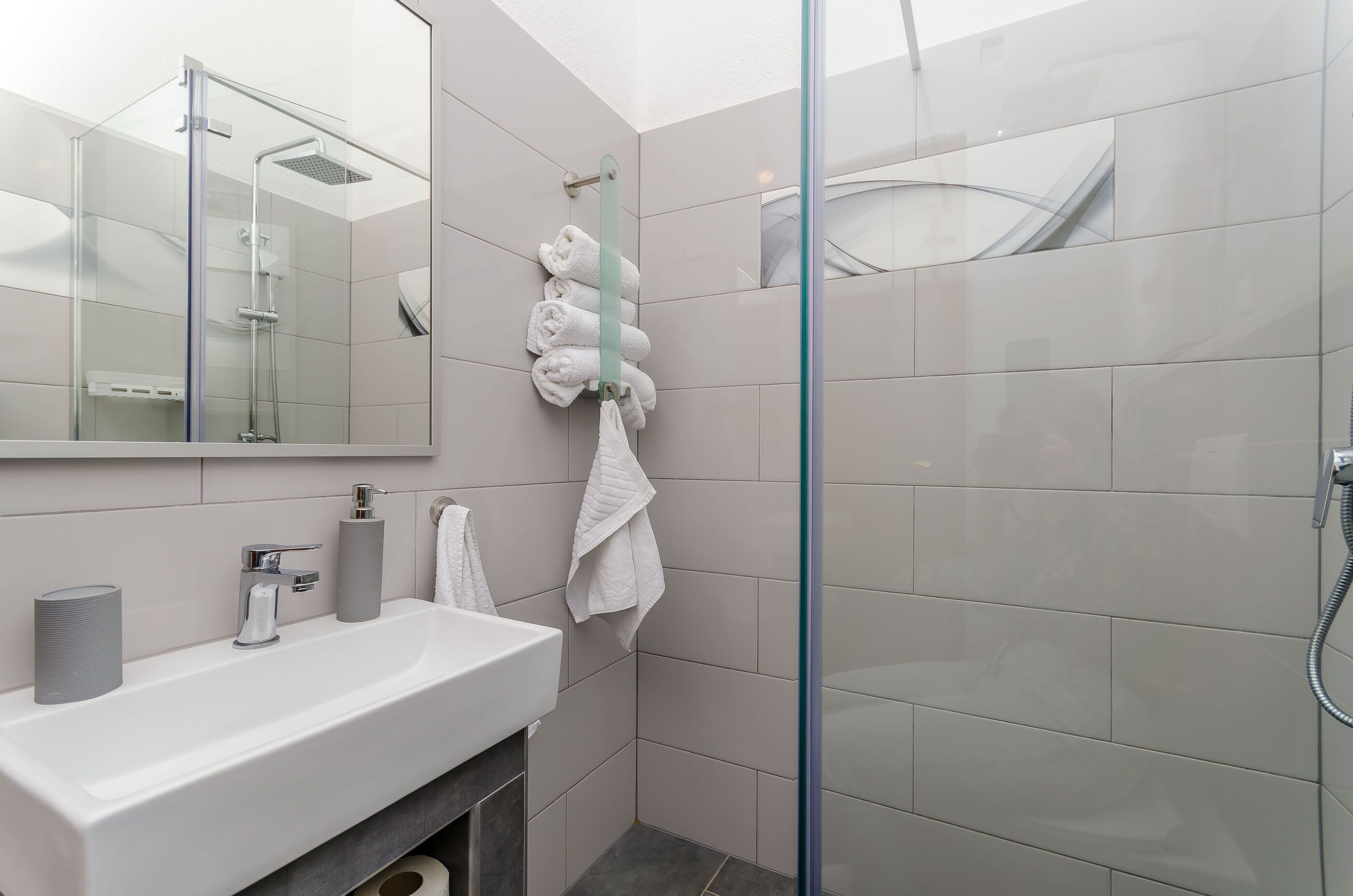 Ein modernes Badezimmer mit einer Duschkabine aus Glas, einem weißen Waschbecken und ordentlich drapierten Handtüchern.