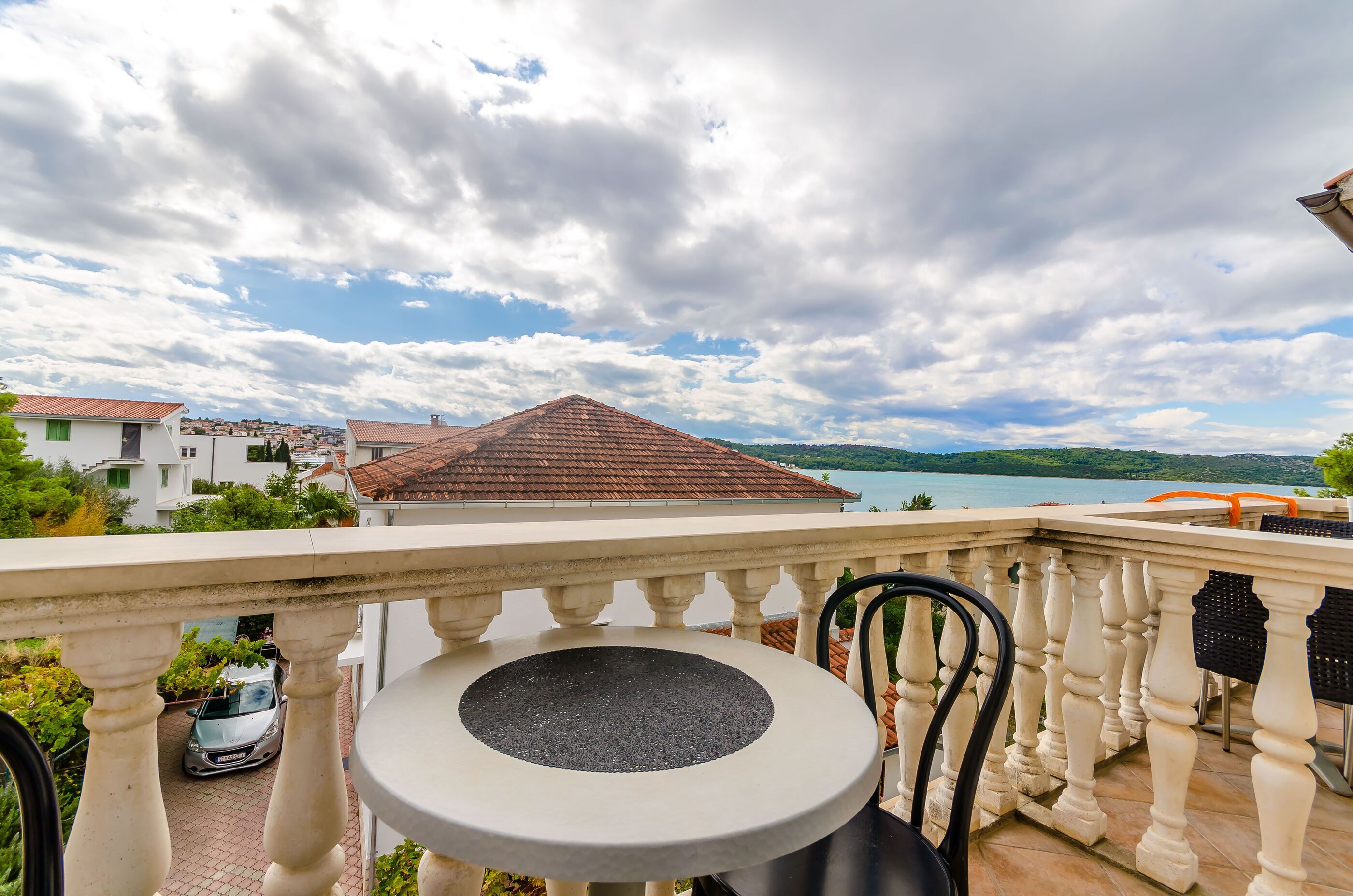 Un balcón con mesa y sillas, con vistas a un paisaje que incluye un lago y edificios.