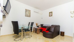 A modern living room with a glass dining table, black chairs, a brown leather sofa, and a small wooden side table. - Apartment Marijana (Trogir)