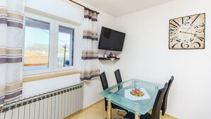 A dining area with a glass table, black chairs, a clock, and a TV mounted on the wall. - Apartment Marijana (Trogir)