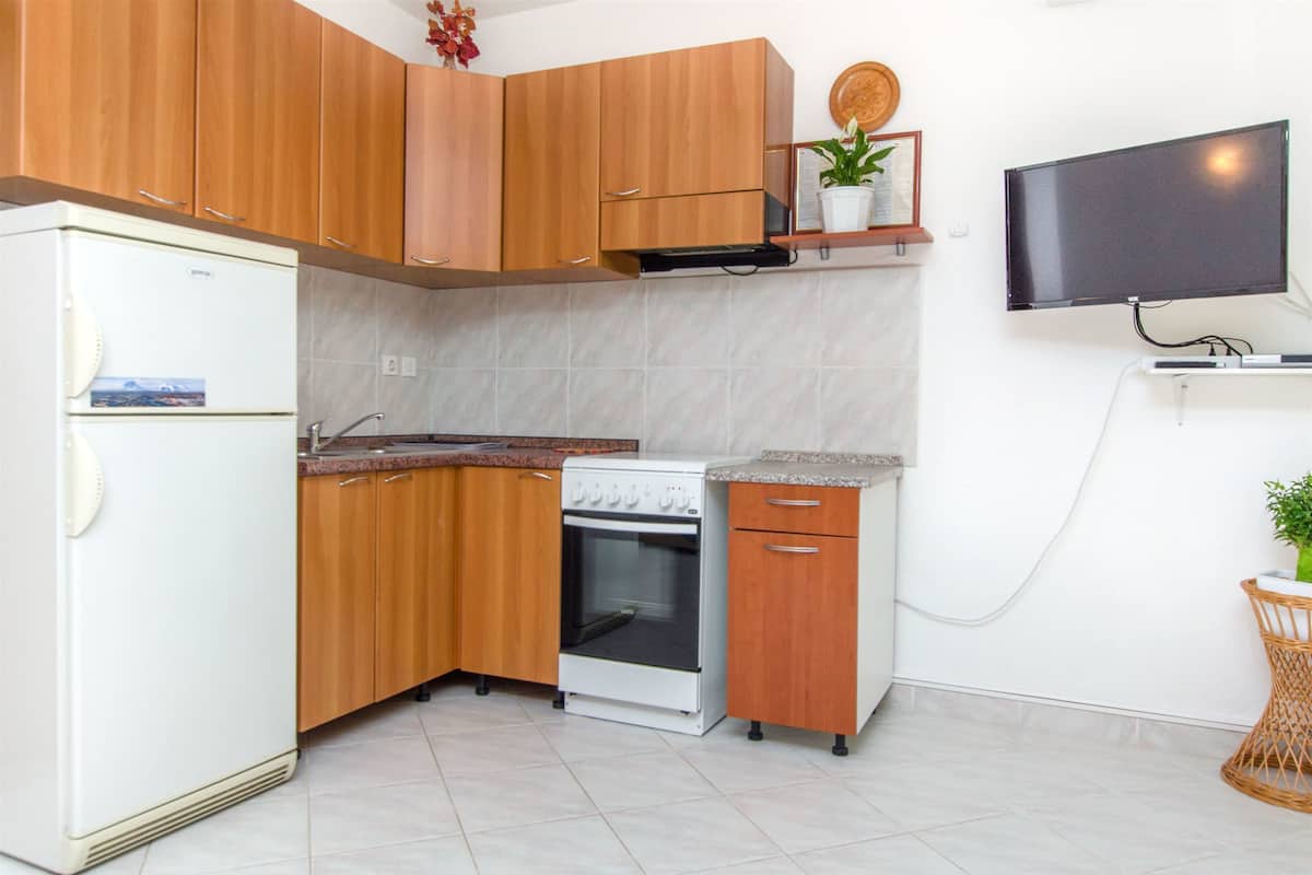 A compact kitchen with wooden cabinets, a white refrigerator, a stove, and a television mounted on the wall.