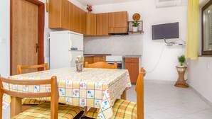 A compact kitchen with wooden cabinets, a refrigerator, a stove, and a dining table with a floral tablecloth. - Apartments Stjepan (Lokva Rogoznica)