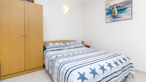 A bedroom with a bed, a wooden wardrobe, a wall-mounted light, and a painting. - Apartments Stjepan (Lokva Rogoznica)