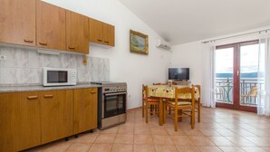 A kitchen with wooden cabinets, a microwave, an oven, and a dining table with chairs. - Apartments Stjepan (Lokva Rogoznica)