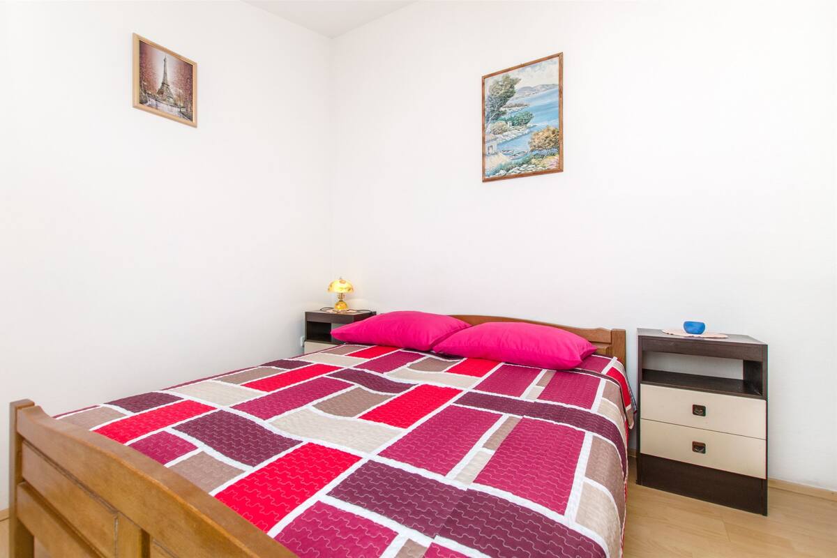A bedroom with a bed, a nightstand, a drawer, and two framed pictures on the wall.