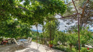 A patio with a table and chairs, surrounded by lush greenery and a view of the sea. - Apartments Stjepan (Lokva Rogoznica)