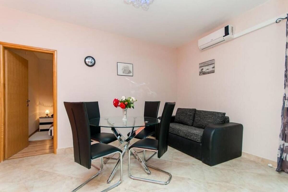 Una sala de estar moderna con una mesa de vidrio, sillas negras, un sofá gris y una mesita auxiliar con un jarrón de flores.