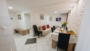 A dining area with a table set for two, a sofa with red cushions, and a television mounted on the wall. - Apartment and Room Old Town (Split)
