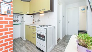 Una cocina compacta con armarios amarillos, una estufa blanca y un horno pequeño. Hay un reloj en la pared y una planta en maceta sobre la encimera.