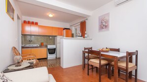Una cocina compacta con armarios naranja, una zona de comedor con sillas de madera y un suelo de baldosas.