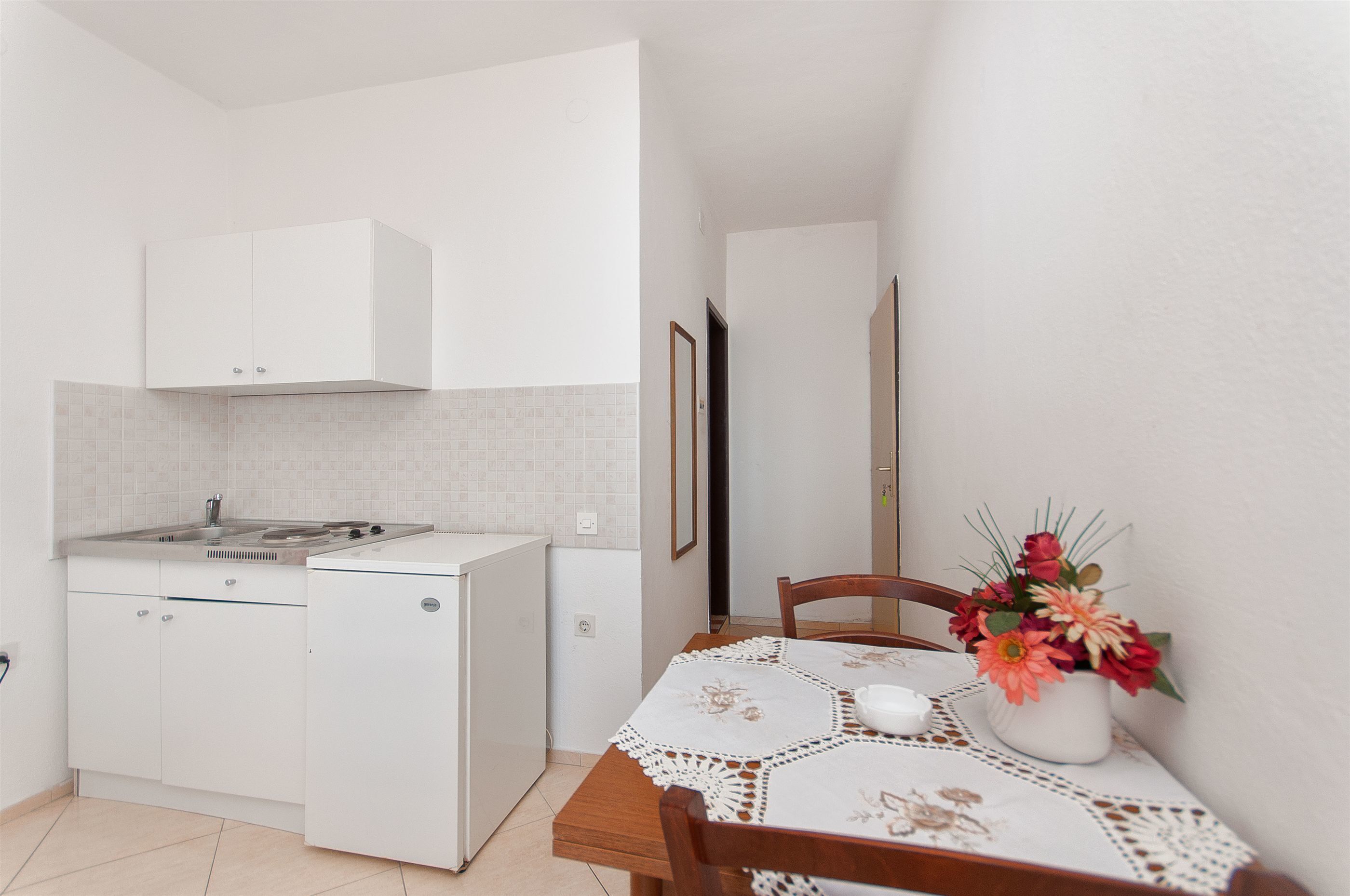 A compact kitchen with white cabinets, a small refrigerator, and a tiled backsplash.
