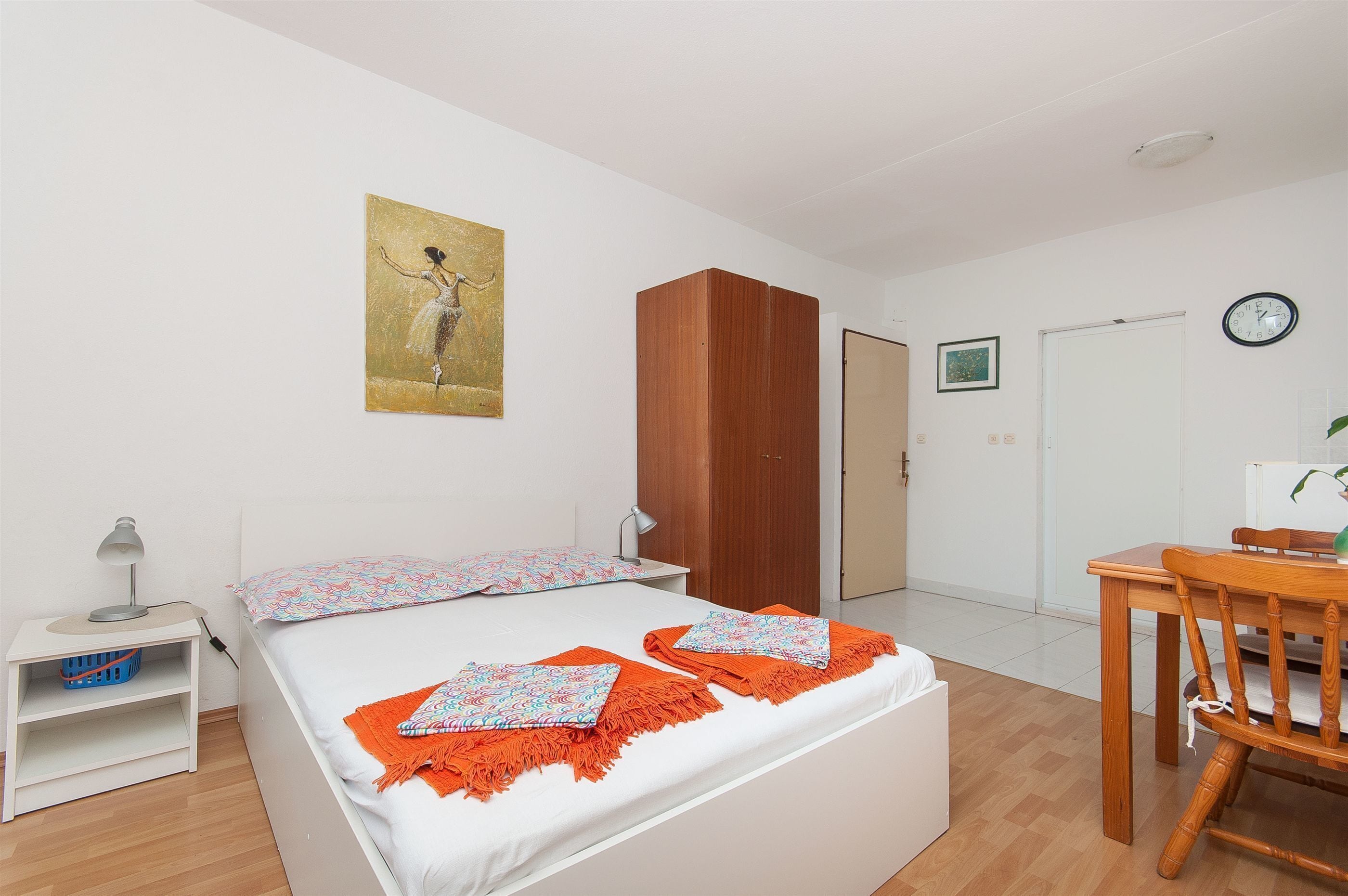 Un dormitorio con cama, un armario de madera, un escritorio con silla, un reloj de pared y un cuadro.