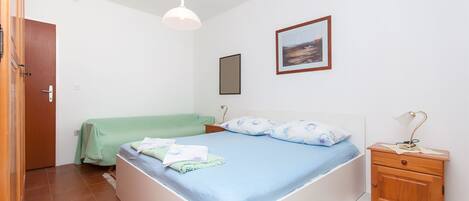 Un dormitorio con cama, mesita de noche, lámpara colgante, un cuadro enmarcado en la pared y una puerta.