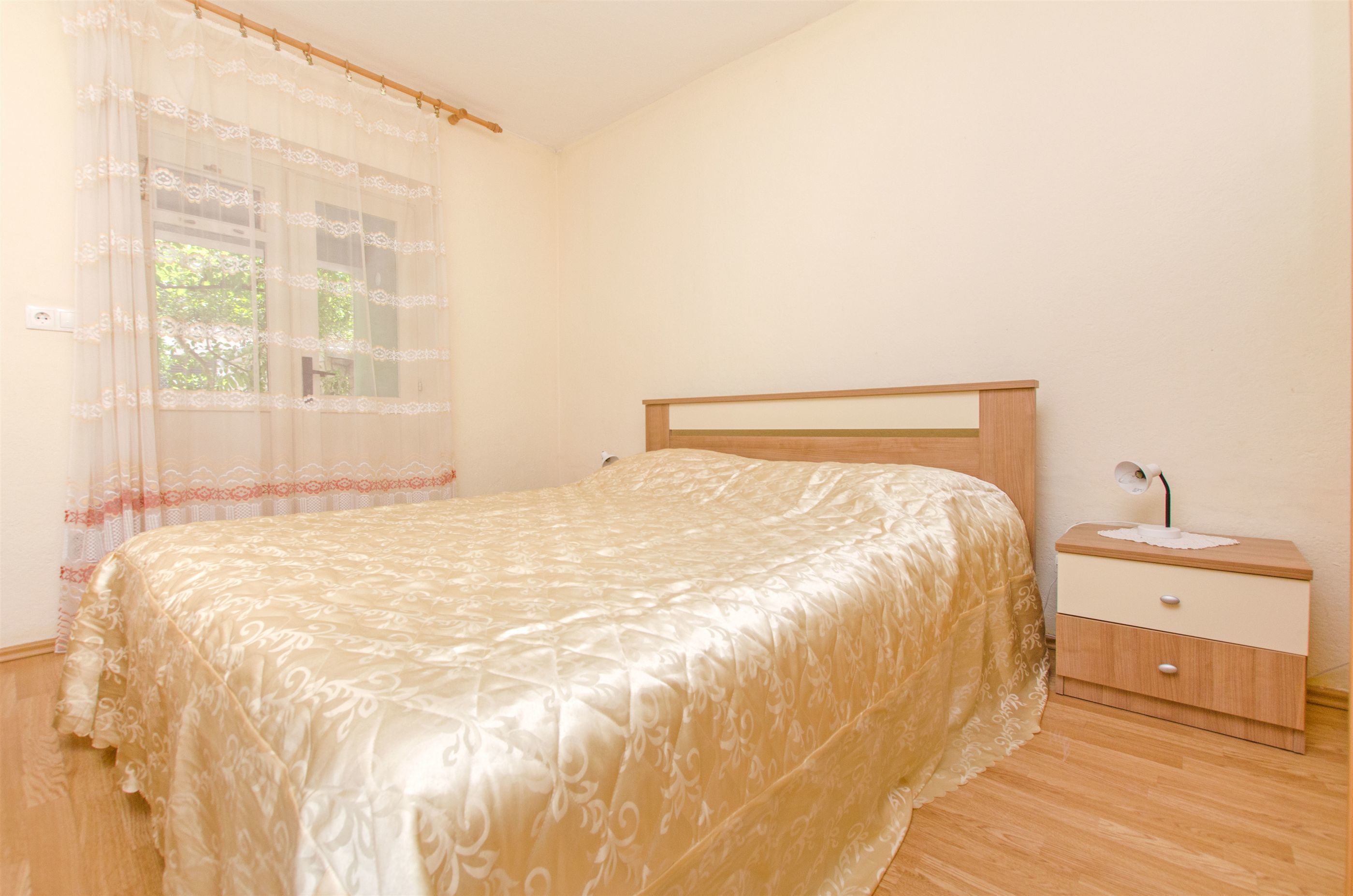 A bedroom with a bed, a nightstand, and a window with a sheer curtain.
