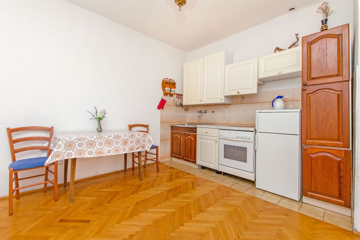 A compact kitchen with wooden cabinets, a white refrigerator, and a dining table with chairs.