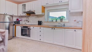 A modern kitchen with white cabinetry, stainless steel appliances, a window with a view of greenery, and a compost bin. - Apartment Leo (Racisce)