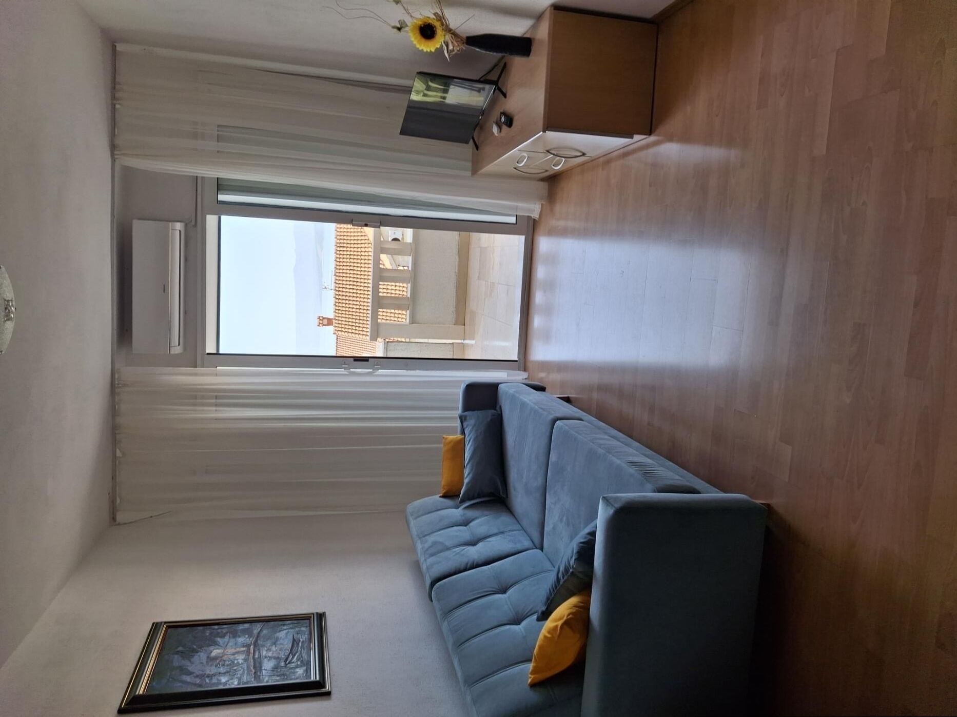A modern living room with a large window, a sofa, and a framed picture on the floor.