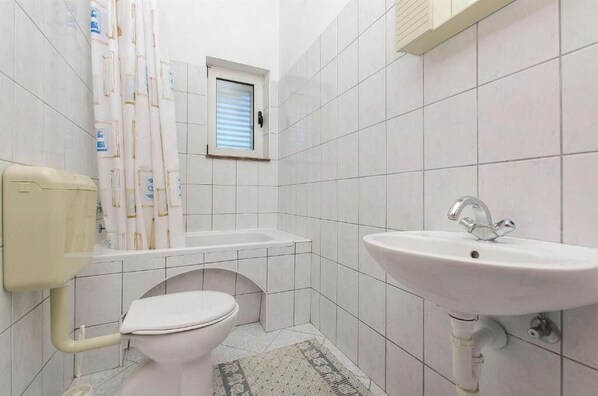 A small, clean bathroom with white tiles, a toilet, a sink, and a shower curtain. - Apartments Nada (Grebastica)