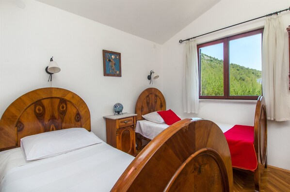 A bedroom with two wooden beds, a nightstand, a lamp, and a window with a view of a green landscape. - Apartments Ana (Prizba)