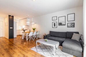 A modern living room with a grey sofa, white coffee table, and a dining area with white chairs.