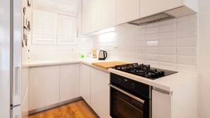 A modern kitchen with white cabinets, a gas stove, an oven, and a window with blinds. - Apartment Apartment In Centre For 6 (Split)
