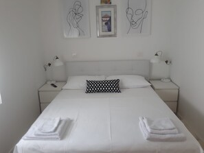 A neatly made bed with white linens and a checkered pillow, two bedside lamps, and a framed picture on the wall.