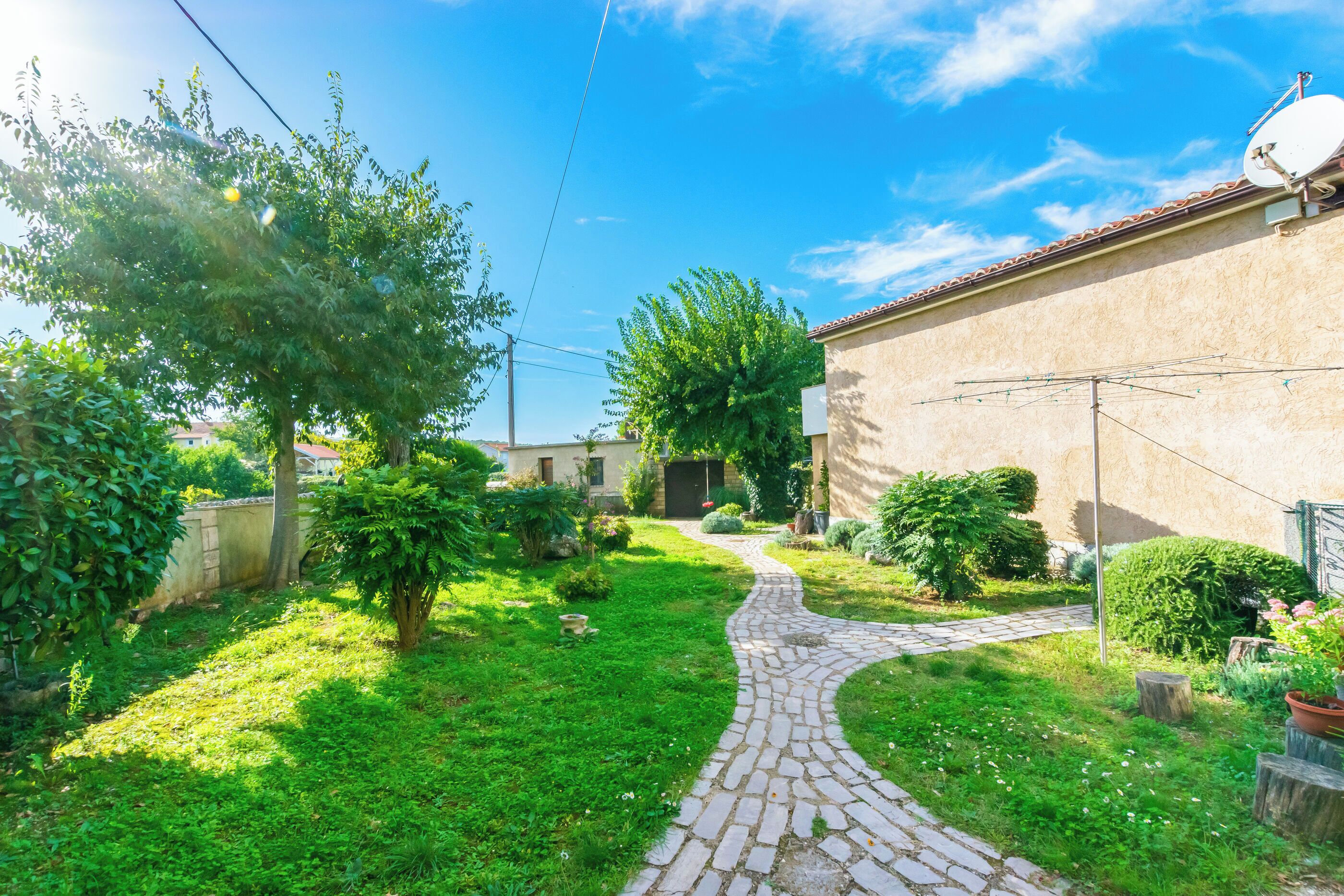 A paved pathway leading to a building with a satellite dish, surrounded by lush greenery and a clear blue sky.