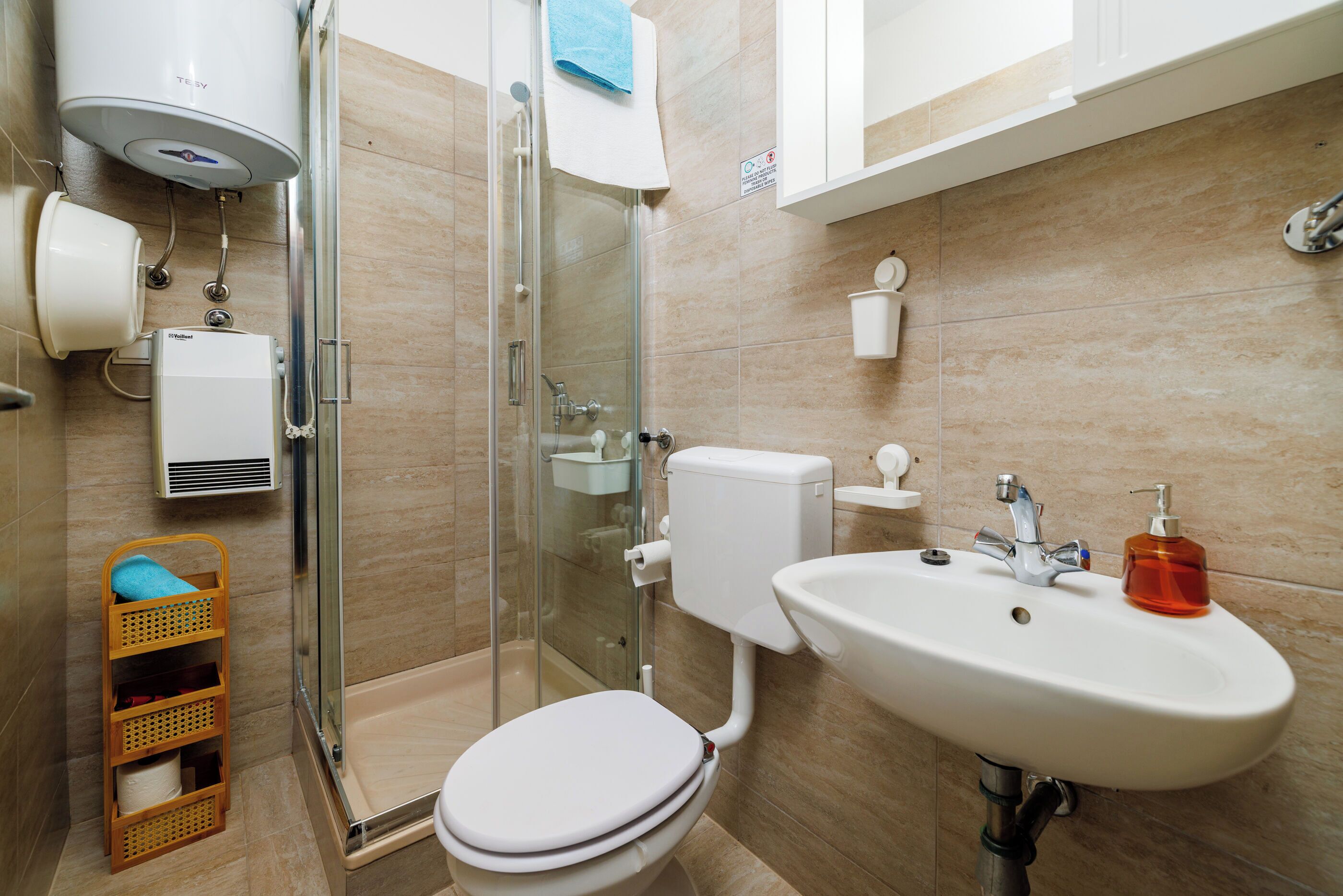 A modern bathroom with a glass-enclosed shower, a toilet, a sink with a soap dispenser, and a towel rack.