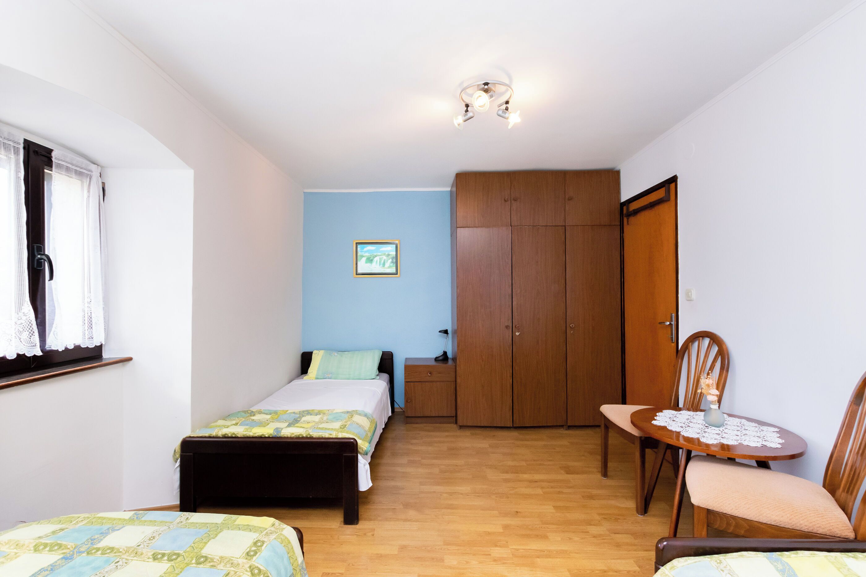 Een slaapkamer met twee bedden, een houten garderobe, een kleine tafel met een vaas en een stoel.