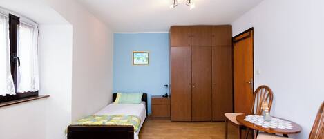 Een slaapkamer met twee bedden, een houten garderobe, een kleine tafel met een vaas en een stoel.