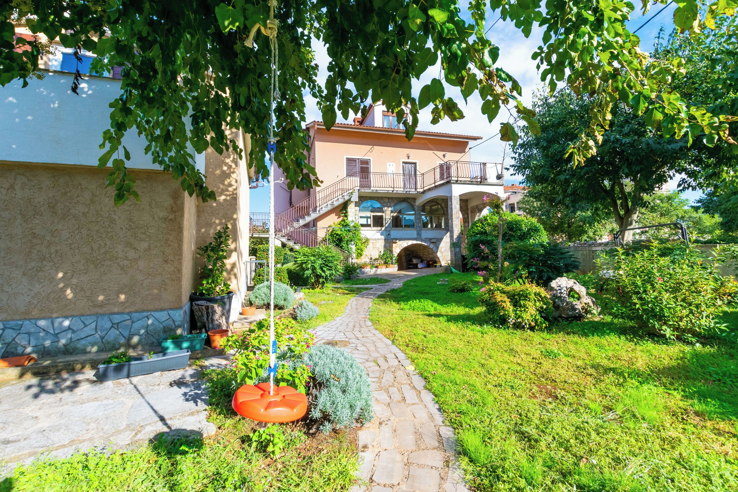A stone pathway leading to a house with a balcony and a stone archway.