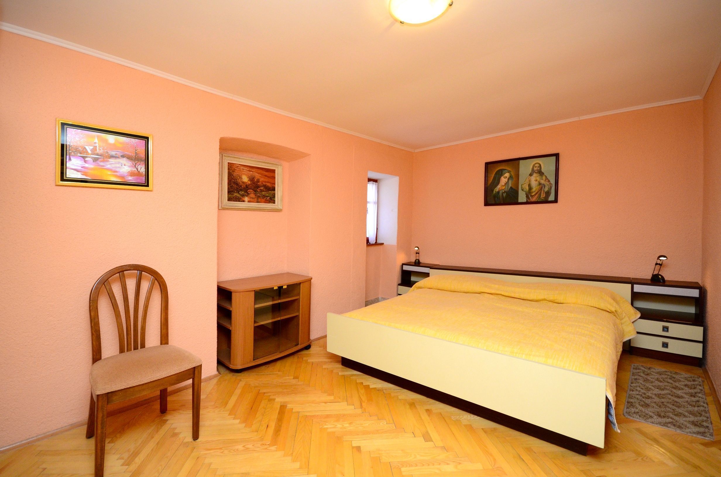 A bedroom with a bed, a chair, a nightstand, and wall art.