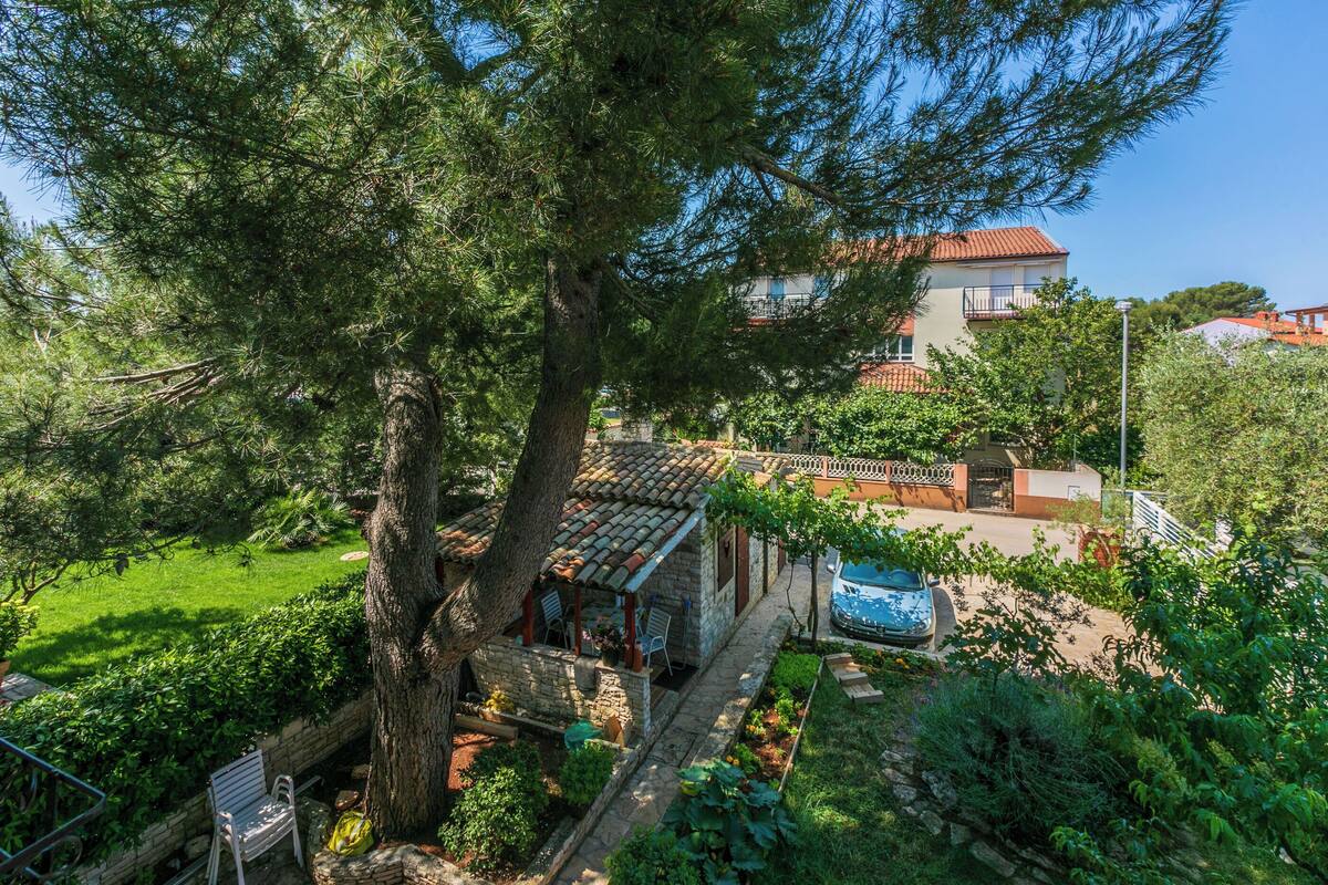 A stone house with a tiled roof, a garden, and a blue car parked outside.