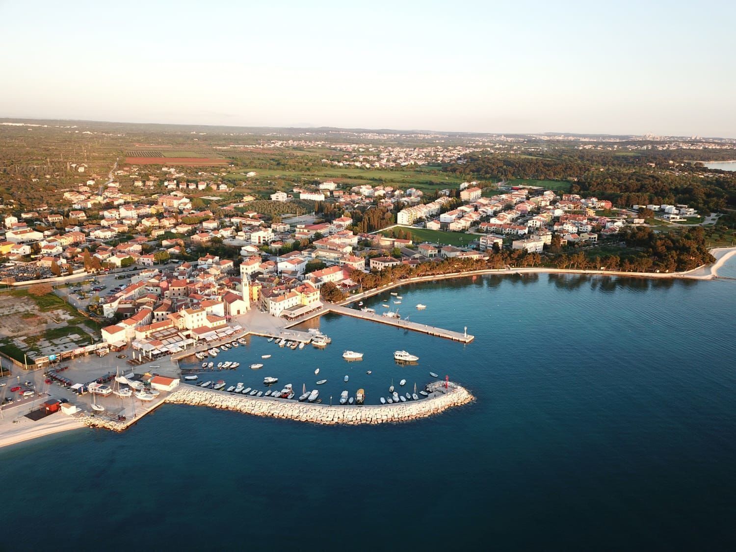 An aerial view of a coastal town with a marina, residential buildings, and a prominent church.