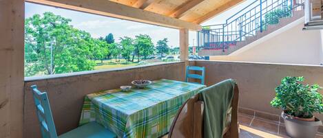 Een balkon met een tafel en stoelen, een plant in pot en uitzicht op groen en een parkeerplaats.