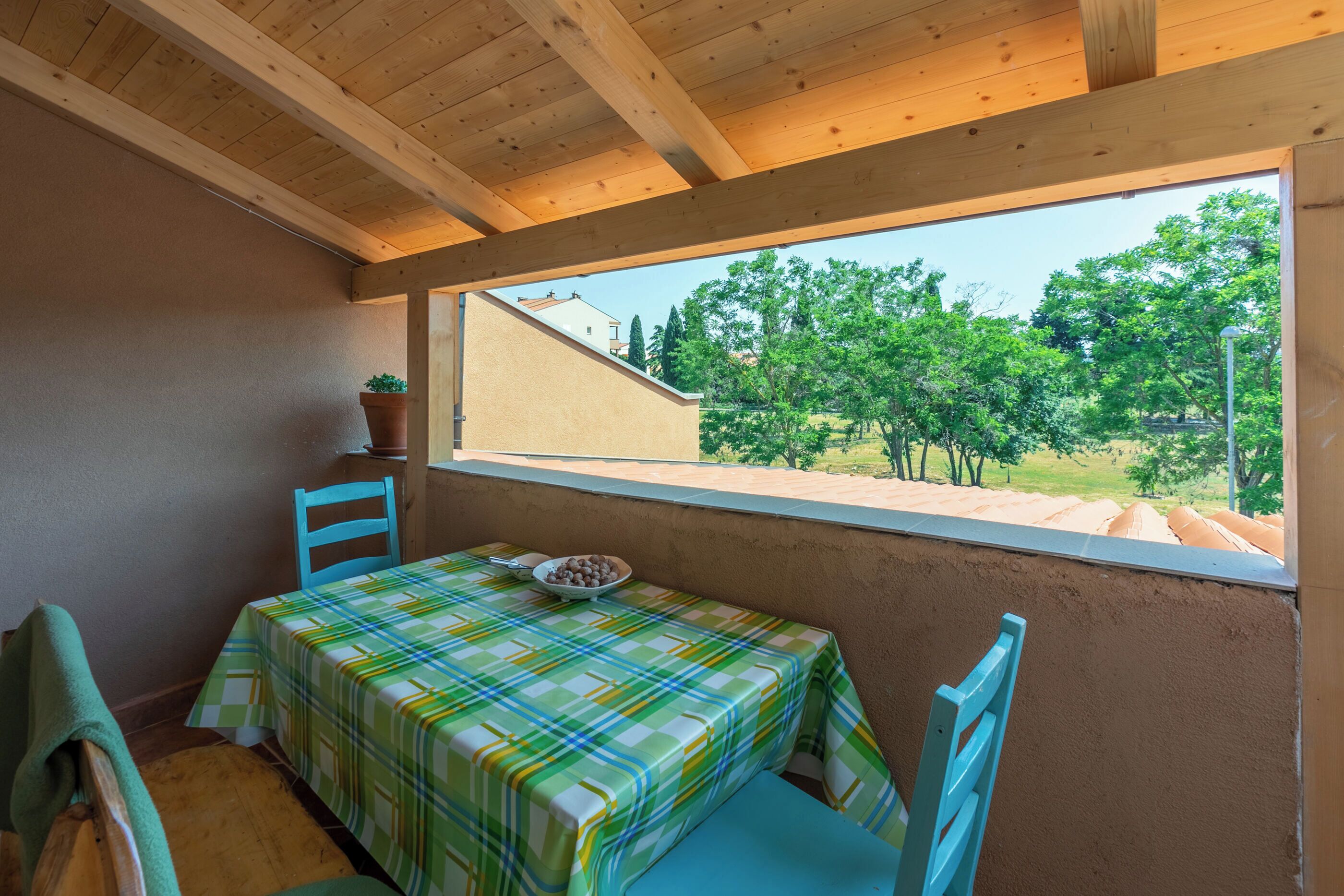 Une petite pièce avec un plafond en bois, une fenêtre donnant sur les arbres, une table recouverte d’une nappe à carreaux et deux chaises.