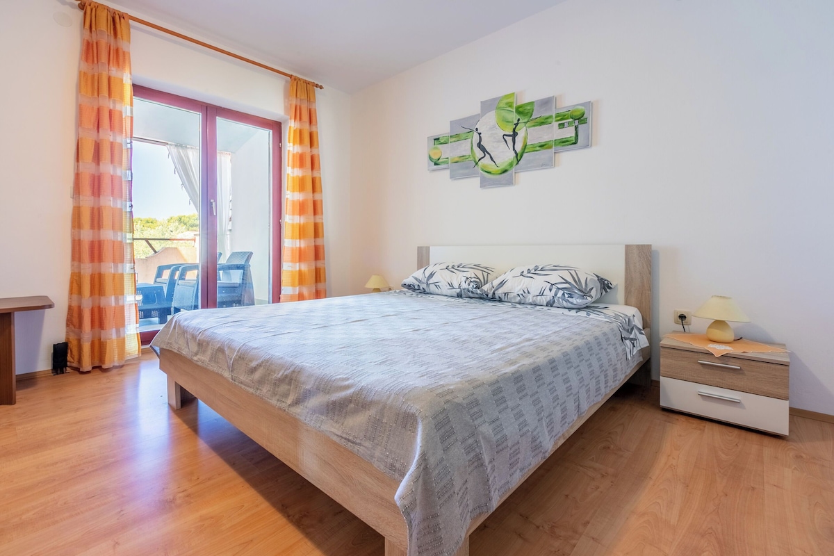 A bedroom with a bed, a nightstand, a lamp, and a window with curtains.