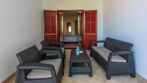 A room with wicker furniture, a bed, and a view through open shutters. - Apartments Armando (Fazana)