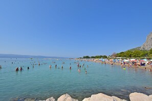 A beach with clear water, people swimming and sunbathing, and a rocky cliff in the background. - Apartment Nansy (Omis)