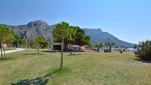 A grassy area with trees, a small building, and mountains in the background. - Apartment Nansy (Omis)