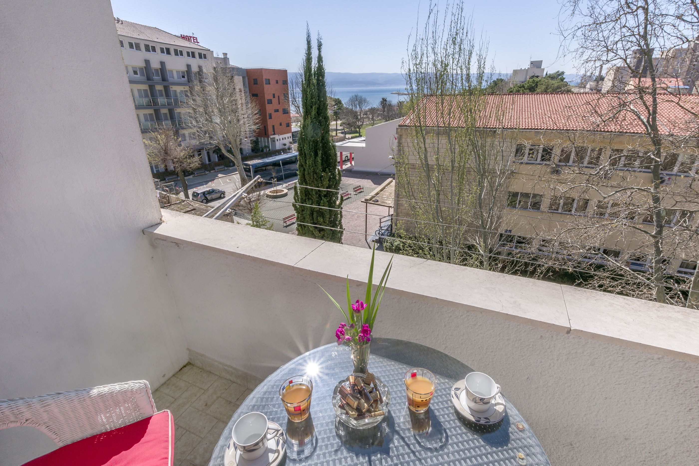 A balcony with a table set for two, a vase with flowers, and a view of the cityscape.