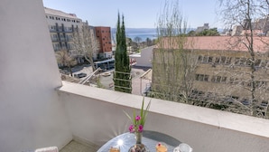 A balcony with a table set for two, a vase with flowers, and a view of the cityscape. - Apartment Nansy (Omis)